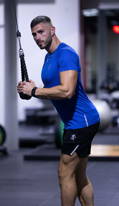 The coach performs a downward tricep pull on a cable machine.